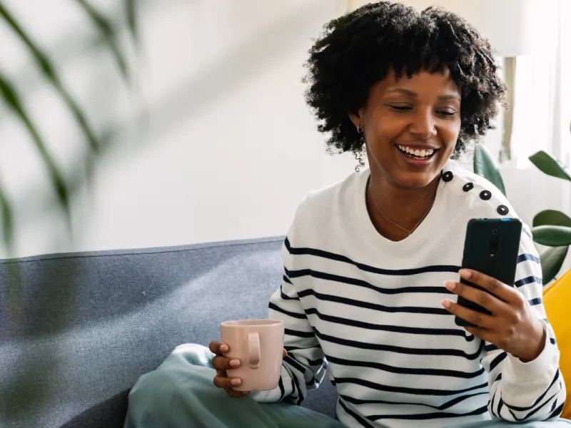 Fröhliche Frau auf dem Sofa mit dem Smartphone