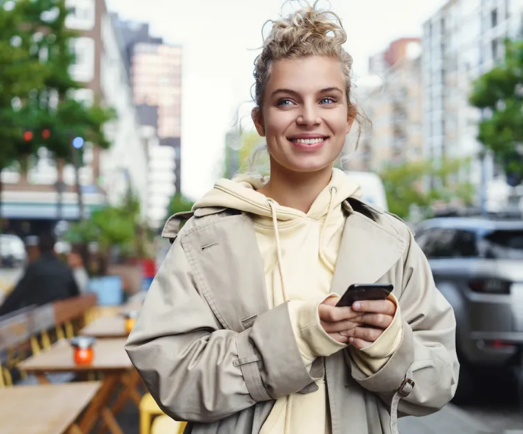Junge Frau freut sich über Nachricht auf Ihrem Smartphone.